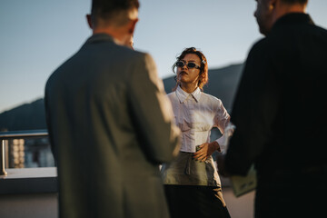 Poster - A diverse group of business people gather on a high-rise balcony, engaging in a creative brainstorming session as the sun sets. They exemplify teamwork and collaboration.