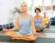 © JackF - There is group Pilates class in studio for people of different ages. Elderly women in company of hatha yoga lovers performs half-lotus pose, Ardha Padmasana