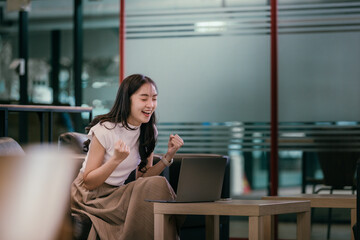 Aufkleber - Young asian businesswoman expressing joy while working remotely on a laptop, celebrating a significant achievement in a stylish modern coworking space filled with natural light
