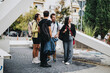 © qunica.com - A diverse group of four young adults casually converse while exploring a modern urban setting. They are surrounded by greenery and architectural elements, creating a vibrant and energetic outdoor