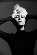 © SHOTPRIME STUDIO - Stylish young woman with short blonde hair posing dramatically, wearing a black turtleneck. Black and white portrait focused on expression and modern fashion.