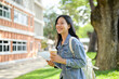 © bongkarn - A beautiful, smiling Asian female college student walks through the university on a bright day.