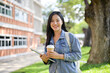 © bongkarn - An attractive Asian female college student stands outdoors at her university, smiling at the camera.