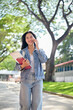 © bongkarn - A cheerful female student enjoys talking on the phone with her friend while on her way to class.