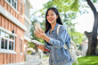 © bongkarn - A happy Asian female college student enjoys a video call while heading to class on campus.