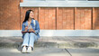© bongkarn - A positive Asian female college student sits on the edge of a footpath, and looking to the side.