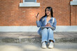 © bongkarn - A positive Asian female student sits on the edge of a footpath, pointing and looking to the side.