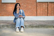© bongkarn - A positive Asian female college student sits on the edge of a footpath, and looking to the side.