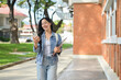 © bongkarn - An attractive Asian woman walks outdoors while reading texts on her smartphone on her way to class.