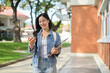 © bongkarn - An attractive Asian woman walks outdoors while reading texts on her smartphone on her way to class.