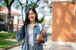 © bongkarn - A beautiful college student showing her smartphone to the camera while standing at the university.