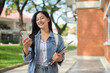 © bongkarn - An attractive Asian woman walks outdoors while reading texts on her smartphone on her way to class.
