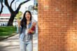 © bongkarn - An Asian female college student stands outdoors, showing a victory fist and smiling at the camera.