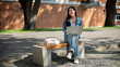 © bongkarn - A positive Asian female college student sits on a bench at her university, using her laptop to work.