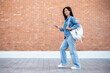 © bongkarn - A side view of a smiling Asian female college student holding her smartphone while walking outdoors