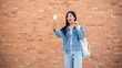 © bongkarn - A cheerful Asian female student talks on a video call through her smartphone while standing outdoors