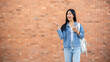 © bongkarn - A smiling woman points at an empty space while standing outdoors with a brick wall in the background