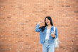 © bongkarn - A smiling woman points at an empty space while standing outdoors with a brick wall in the background