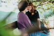 © qunica.com - A young couple shares a joyful and intimate moment while sitting on a wooden bench in a green, leafy outdoor setting.