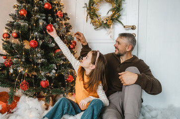 Wall Mural - A father and daughter happily decorate the Christmas tree together. A sweet moment of family celebration