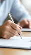 © Exnoi - Close-up of a Person's Hand Holding a Pen While Writing Notes on a Notebook at a Desk in a Bright Indoors Environment with Soft Lighting and Focused Expression