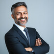 © PRASANNAPIX - A professional profile photo of an Indian business man wearing suit and tie, smiling with arms crossed on grey background.