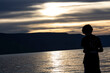 © Salouw - a person standing on the shore of a lake at sunset