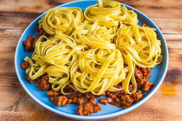 Wall Mural - Spaghetti Bolognese pasta nests with Bechamel sauce and minced beef fried with tomatoes, onions and carrots on a blue plate on a wooden table. Top view. Copyspace or space for text.