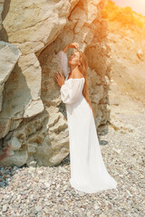 Wall Mural - A woman in a white dress is standing on a rocky beach. Concept of serenity and tranquility, as the woman is enjoying the natural beauty of the beach.