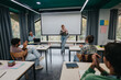 © qunica.com - Female student stands confidently in front of classmates, delivering a project presentation in a modern classroom with attentive audience and discussion.