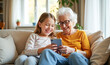 © Radorog. - grandmother and granddaughter with phones in their hands are sitting on the couch laughing