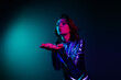 © deagreez - Portrait of stunning young woman send air kiss empty space wear shiny dress neon light dark blue background