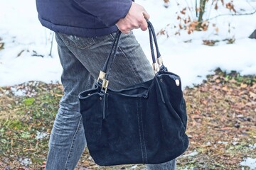 Wall Mural - man in jacket and gray jeans holds in hand on side one elegant with handles leather black women's with iron shiny fittings and zippers glamorous handbag daytime on street