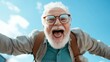 © Maximages  - An elderly man with glasses and white beard enthusiastically reaches towards the camera, exuding excitement and adventure, set against a clear sky background.