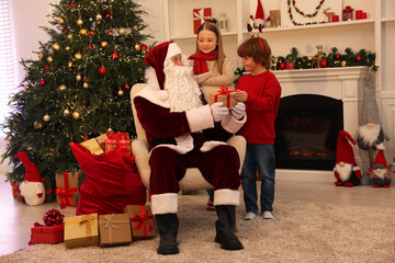 Wall Mural - Christmas celebration. Santa Claus giving gift box to kids at home