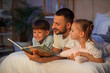 © Pixel-Shot - Father and his children reading book on bed in room