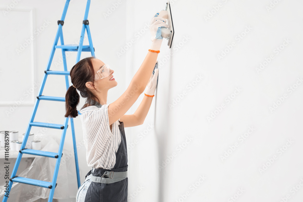 Female worker with putty knife doing repair in room
