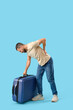 © Pixel-Shot - Young man with suitcase suffering from back pain on blue background