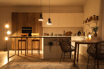 Wall Mural - Interior of modern kitchen with tables, counters and glowing lamps in evening