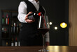 © New Africa - Professional sommelier pouring red wine into glass at wooden table indoors, closeup