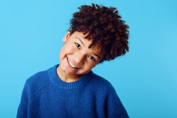 Cheerful young african american boy with curly hair beaming with joy against a vibrant blue background