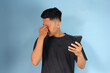 © Lailar Studio - Young Asian man looking at mobile phone with sad expression while holding head