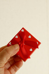 Wall Mural - A hand holds a small red gift box decorated with white hearts and tied with a satin red bow against a white background.