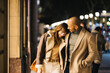 © Jordi Salas - A loving couple shares a joyful moment while strolling down a city street by night. They're enjoying a shopping excursion smiling and embracing intimately.