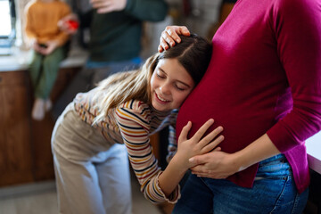 Wall Mural - Daughter hugging, touching pregnant mother's belly. Little girl is looking at mom's belly with love