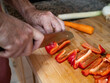 © Beatriz Herrera - Hands of a man skillfully chop fresh bell peppers on a wooden cutting board in a cozy kitchen.