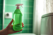 © Andrey - Hand holding a green plastic spray bottle of cleaning product in a bathroom with green tiles