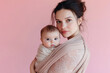 © Lazy_Bear - Young mother holding her newborn baby in sling against pink background. Tender moment in parenthood