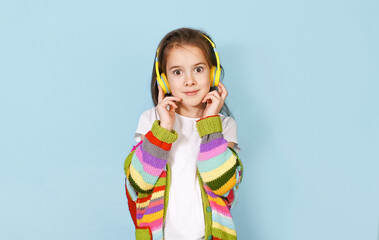 a young girl wearing bright yellow headphones and a colorful striped cardigan looks directly at the 