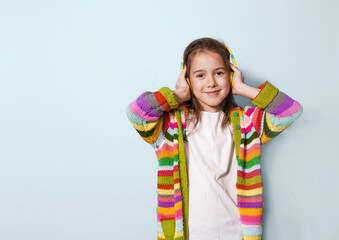 a happy young girl wearing a brightly colored striped cardigan and yellow headphones smiles at the c